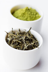Dry leaves of green tea leaves and matcha tea powder in white bowls