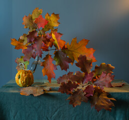 Branch with autumn leaves in a vase. Autumn colors on the leaves. Ripe small pumpkin.