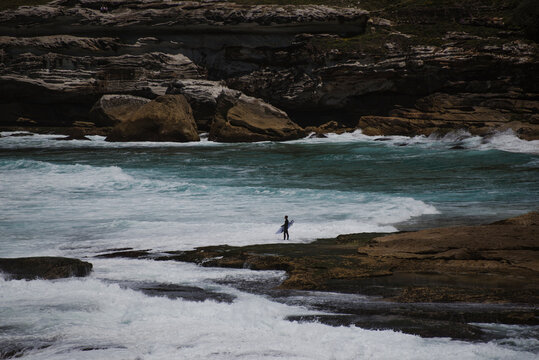 Surfista aspetta sulla rocca per entrare in acqua vicino a Tamarama beach, Sydney