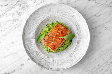 Grilled salmon fillet in avocado sauce in a festive plate on a marble background. Restaurant banquet menu.