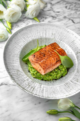 Grilled salmon fillet in avocado sauce in a festive plate on a marble background. Restaurant banquet menu.