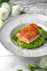 Grilled salmon fillet in avocado sauce in a festive plate on a marble background. Restaurant banquet menu.
