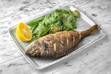 Dorado grilled fish with spinach salad and cheese in a festive plate on a marble background. Restaurant banquet menu.