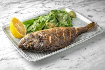 Dorado grilled fish with spinach salad and cheese in a festive plate on a marble background. Restaurant banquet menu.