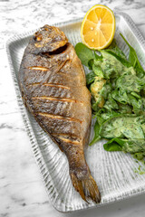 Dorado grilled fish with spinach salad and cheese in a festive plate on a marble background. Restaurant banquet menu.