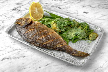 Dorado grilled fish with spinach salad and cheese in a festive plate on a marble background. Restaurant banquet menu.