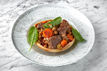 Roast beef or pork with potatoes and carrots in a festive plate on a marble background. Restaurant banquet menu.