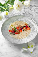 Hearty and healthy breakfast porridge with berries in a festive plate on a marble background. Restaurant banquet menu.