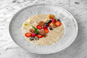 Hearty and healthy breakfast porridge with berries in a festive plate on a marble background. Restaurant banquet menu.