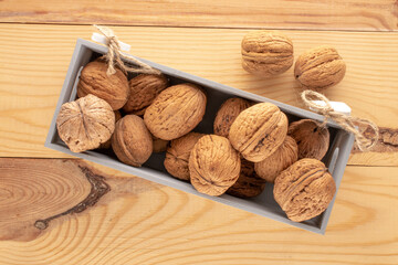 Several ripe delicious walnuts in a wooden box on a wooden table, close-up, top view.