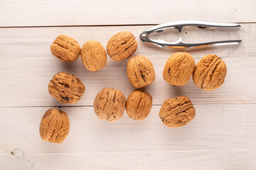 Several ripe delicious walnuts with a metal nutcracker on a wooden table, close-up, top view.