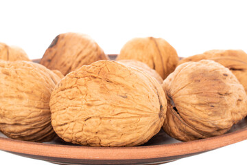 Several ripe delicious walnuts on a clay plate, close-up, isolated on white.