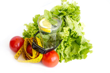 A glass of water, lettuce, tomatoes, a tape measure and a fitness bracelet on a white background. The concept of healthy food and active lifestyle. - 477860901