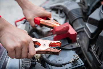 Fototapeta premium Unrecognizable woman using battery cable to recharge her vehicle battery.