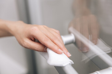 Obraz na płótnie Canvas Cleaning glass door handles with an antiseptic wet wipe. Woman hand using towel for cleaning home room door link. Sanitize surfaces prevention in hospital and public spaces against corona virus