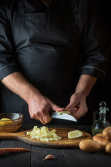 Before preparing the national dish, the chef cuts raw potatoes into small pieces with a knife. Close-up of a cook hands while working in a restaurant kitchen