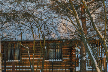 Fototapeta na wymiar winter landscape. A wooden house covered with snow behind a fence, next to trees.
