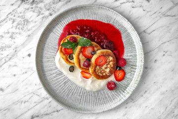 Cheese cakes with condensed milk and berries in a festive plate on a marble background. Restaurant banquet menu.
