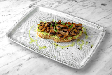 Bruschetta with guacamole and fried mushrooms in a festive plate on a marble background. Restaurant banquet menu.
