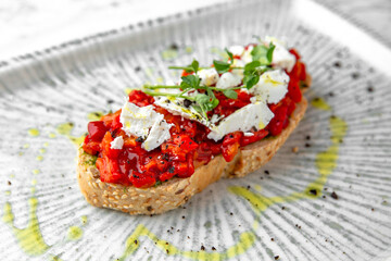 Bruschetta with baked peppers and tomatoes in a festive plate on a marble background. Restaurant banquet menu.