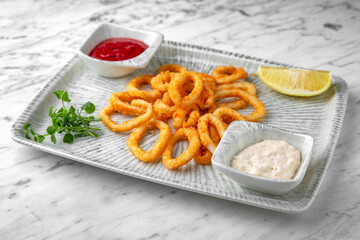 Onion or squid rings with sauce in a festive plate on a marble background. Restaurant banquet menu.