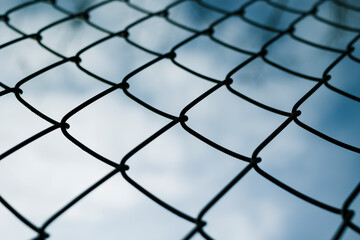 Fototapeta premium Dramaic blue sky with white clouds through a metal grid chain fence . low angle view