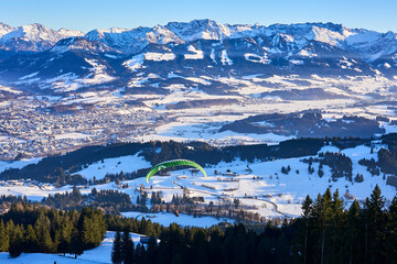 Sonthofen, Bavaria, Germany, 12-17-2021, paraglider starting from Mittag summit into the snowy landscape of Iller Valley near Sonthofen and Oberstdorf 