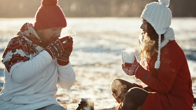Man and woman on date meeting christmas. Young couple in love kiss in first snowy winter day and drink tea. Happy people smiling and flirting while snow falling. Happiness, relationship concept