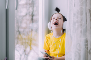 A boy with a phone is sitting on a lifestyle window . Social media. Modern children. An article about developed children.