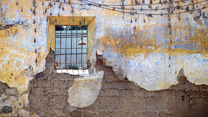 blue yellow decaying wall with small barred window