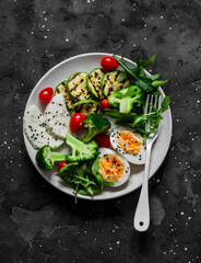 Vegetarian breakfast, snack bowl - salad mixed vegetables, boiled egg, grilled zucchini, cheese on a  dark background, top  view