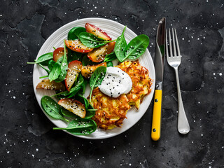 Potato latkes with baked apples, spinach salad on a dark background, top view. Delicious breakfast, snack, vegetarian lunch