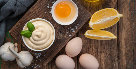 Fresh mayonnaise, eggs, butter and lemon on a wooden background. Side view, copy space. Homemade mayonnaise, white sauce.