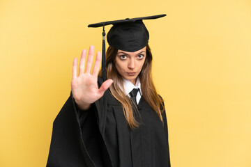 Young university graduate isolated on yellow background making stop gesture