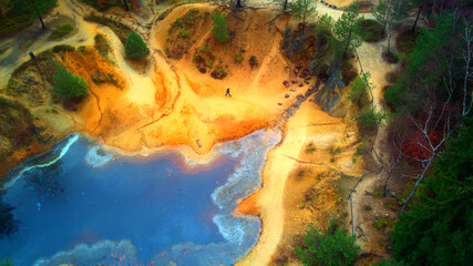 Fototapeta na wymiar Aerial view of lake in the middle of wood. Top down view with beautiful colours on water surface, rocks and trees.