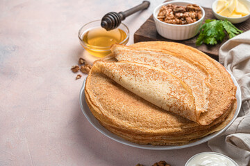 Traditional pancakes on a light background with honey, sour cream and nuts. Pancake day. Side view, copy space.