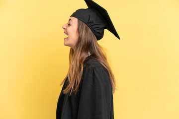 Young university graduate isolated on yellow background laughing in lateral position