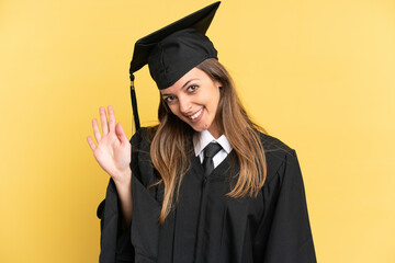 Young university graduate isolated on yellow background saluting with hand with happy expression