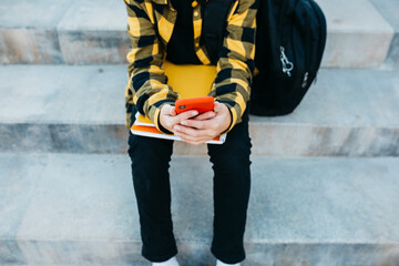 Close up of Teenager's hands using a red smartphone and sitting on stairs - obrazy, fototapety, plakaty