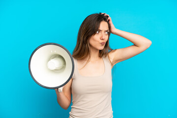 Young caucasian woman isolated on blue background holding a megaphone and having doubts