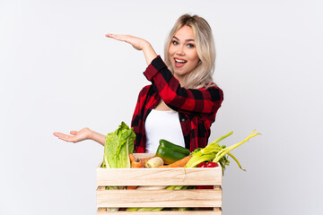 Farmer girl holding a basket full of fresh vegetables over isolated white background holding...