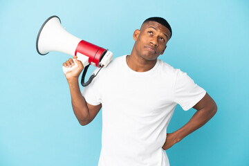Young latin man isolated on blue background holding a megaphone and thinking