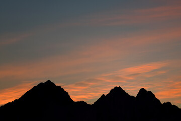 Colorful sunrise behind silhouette of rugged mountain peaks.