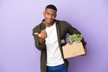 Latin man making a move while picking up a box full of things inviting to come with hand. Happy...