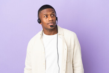 Telemarketer latin man working with a headset isolated on purple background thinking an idea while looking up