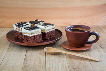 Pieces of delicious chocolate cake with cream and chocolate fondant in a plate and a cup of coffee on a wooden table