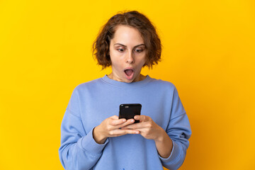 Young English woman isolated on pink background looking at the camera while using the mobile with surprised expression