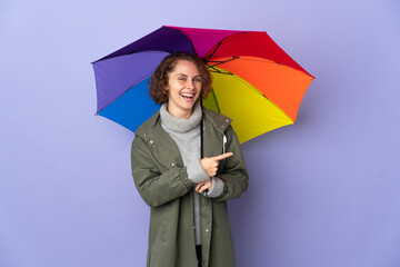 English woman holding an umbrella isolated on purple background pointing finger to the side