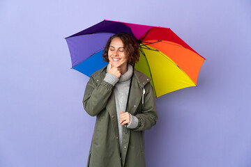 English woman holding an umbrella isolated on purple background looking to the side and smiling