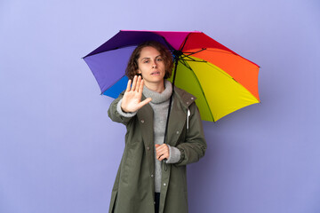 English woman holding an umbrella isolated on purple background making stop gesture